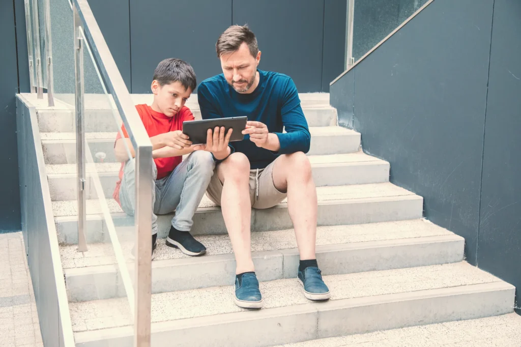 Pai e filho olhando o celular numa escada da quadra