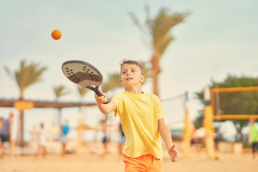 Menino rebate a bola na quadra de areia